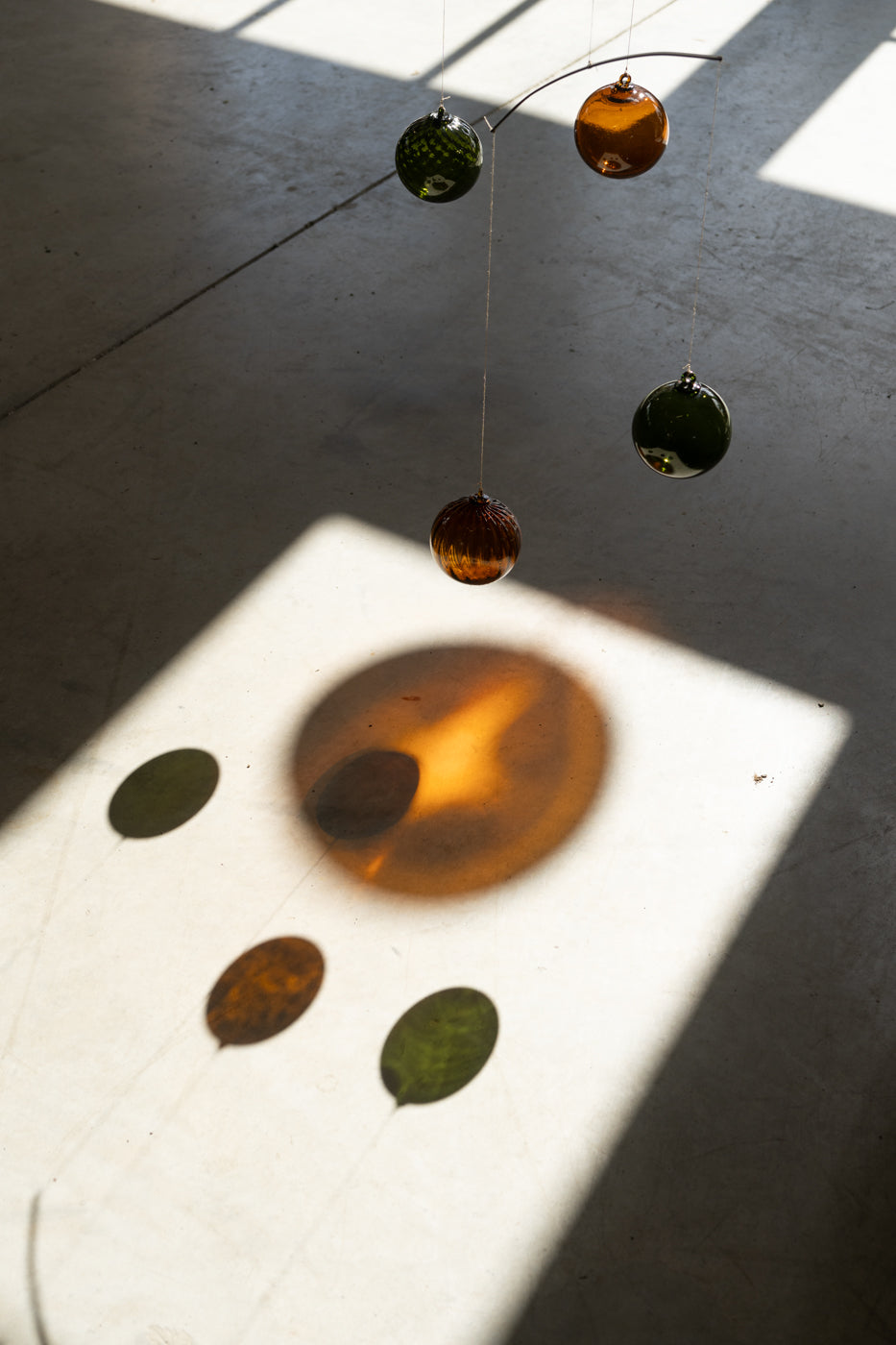 reflets lumineux ambrés et verts sur le sols des boules à suspendre en géoverrerie de la marques Ostraco