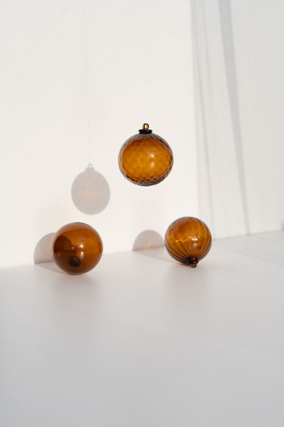 Trois boules de Noël en verre soufflé ambré, simple, côtelée et ananas, l’une suspendue et deux posées au sol